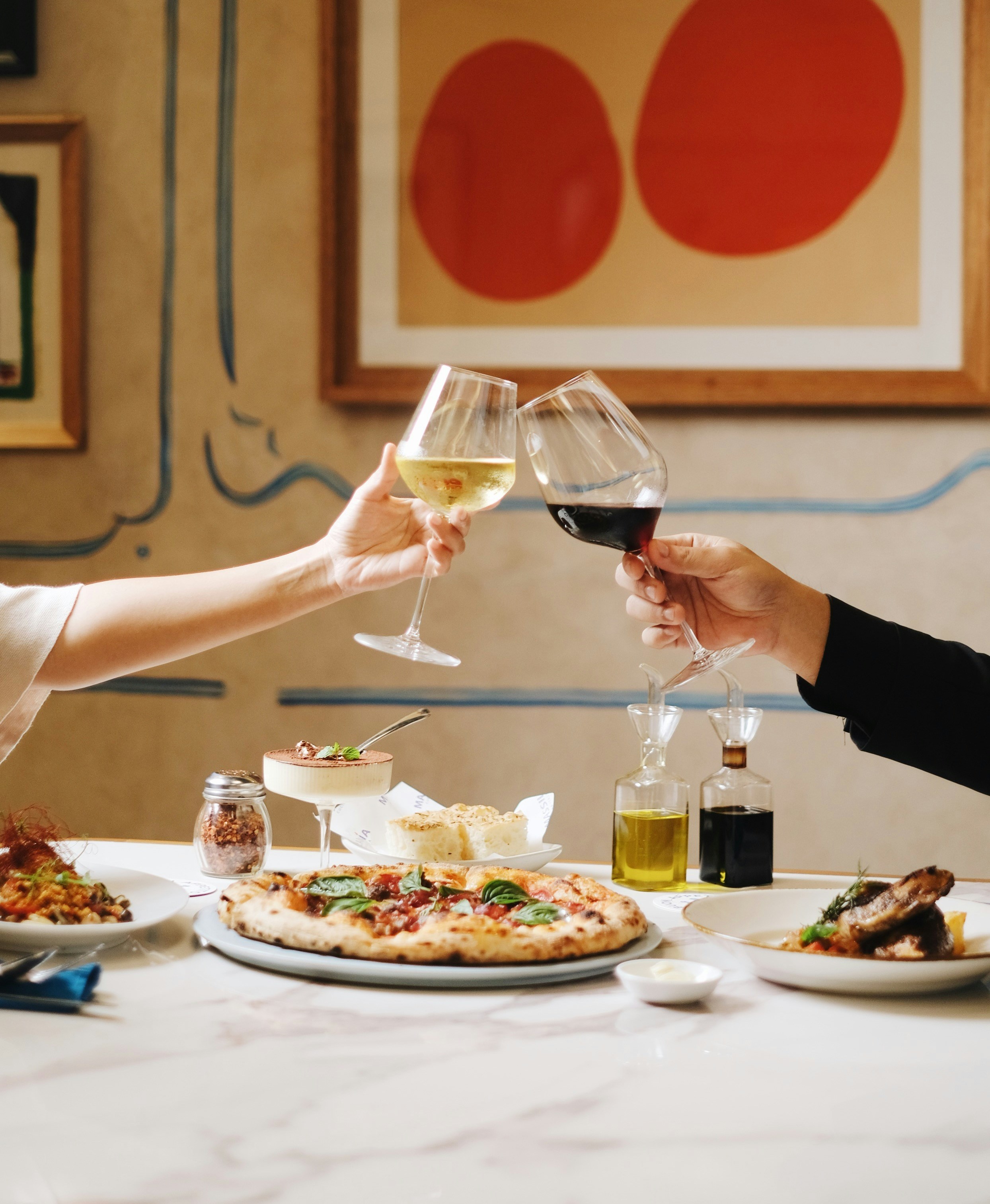 Zwei Personen stoßen mit Wein an, Pizza auf dem Tisch.