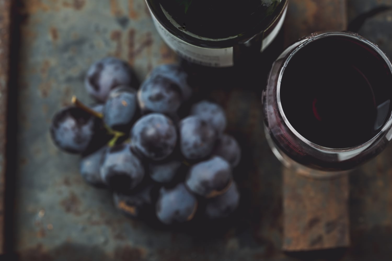 Flasche Rotwein, ein gefülltes Weinglas und Weintrauben von oben