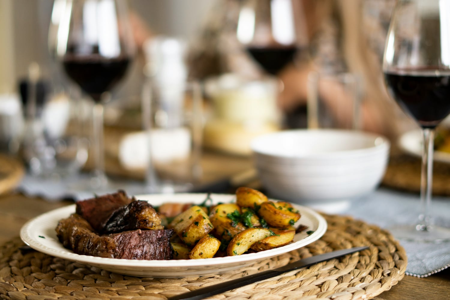 Teller mit Steak und Bratkartoffeln mit gefüllten Weingläsern mit Rotwein