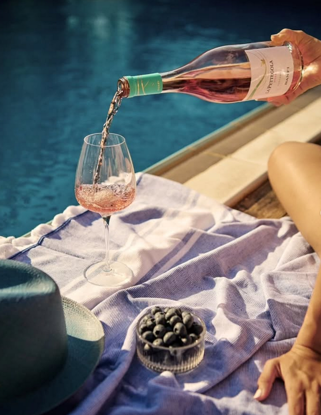 Frau füllt Banfi La Pettegola Rosé am Pool in Weinglas